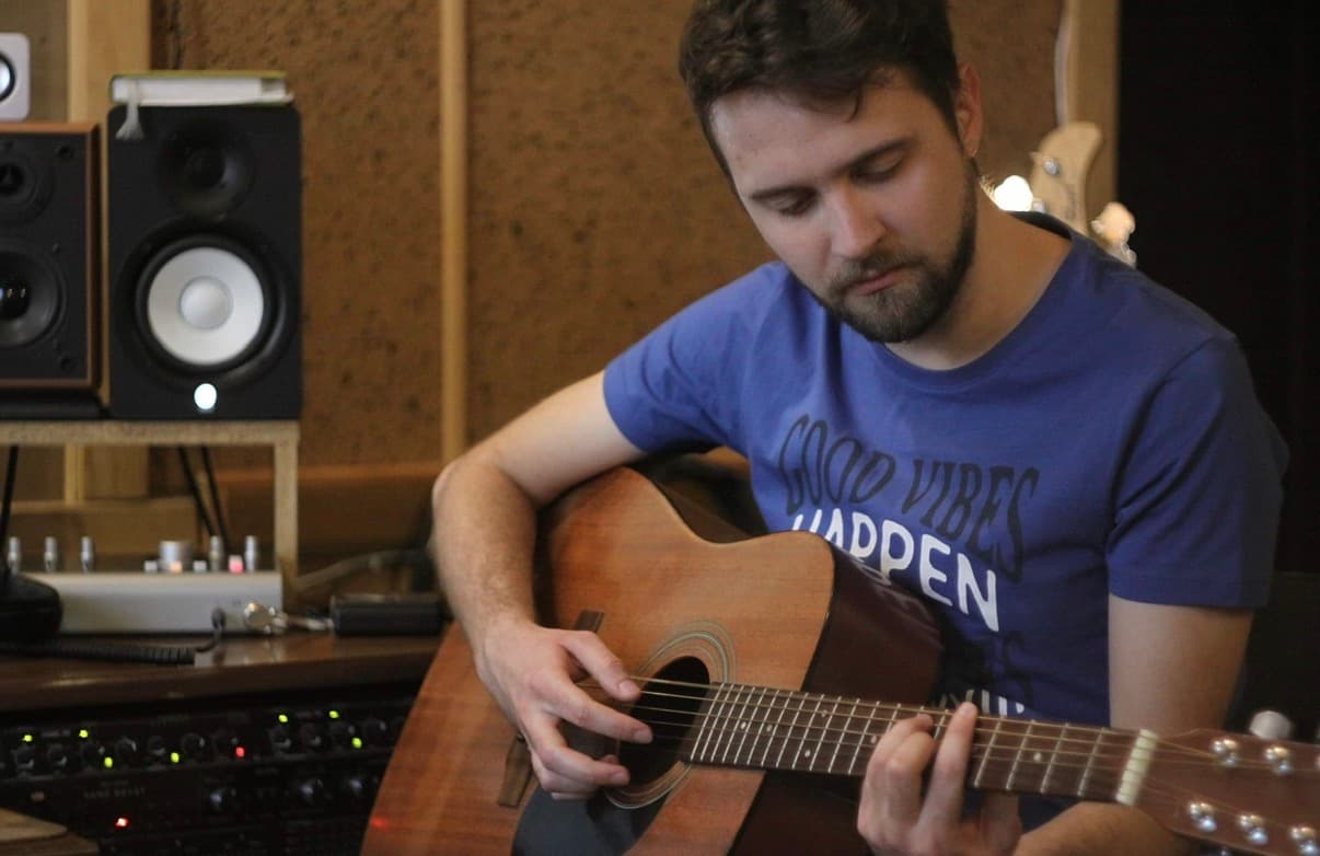 Roman Moroz playing an acoustic guitar in a recording studio.
